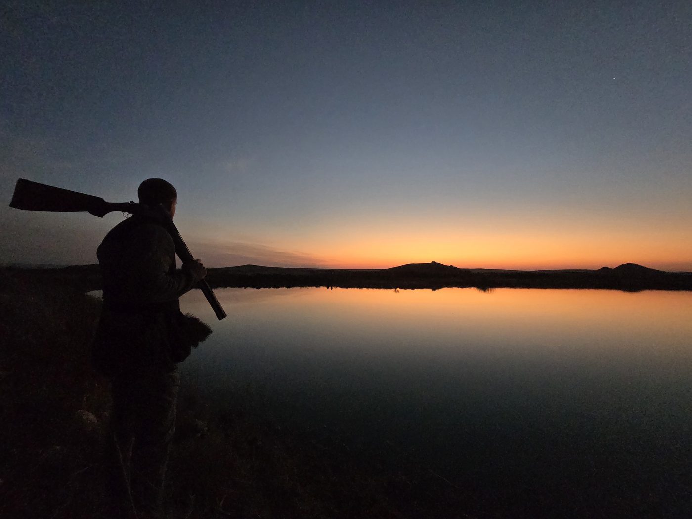 Hunter silhouetted against a Karoo sunset over water